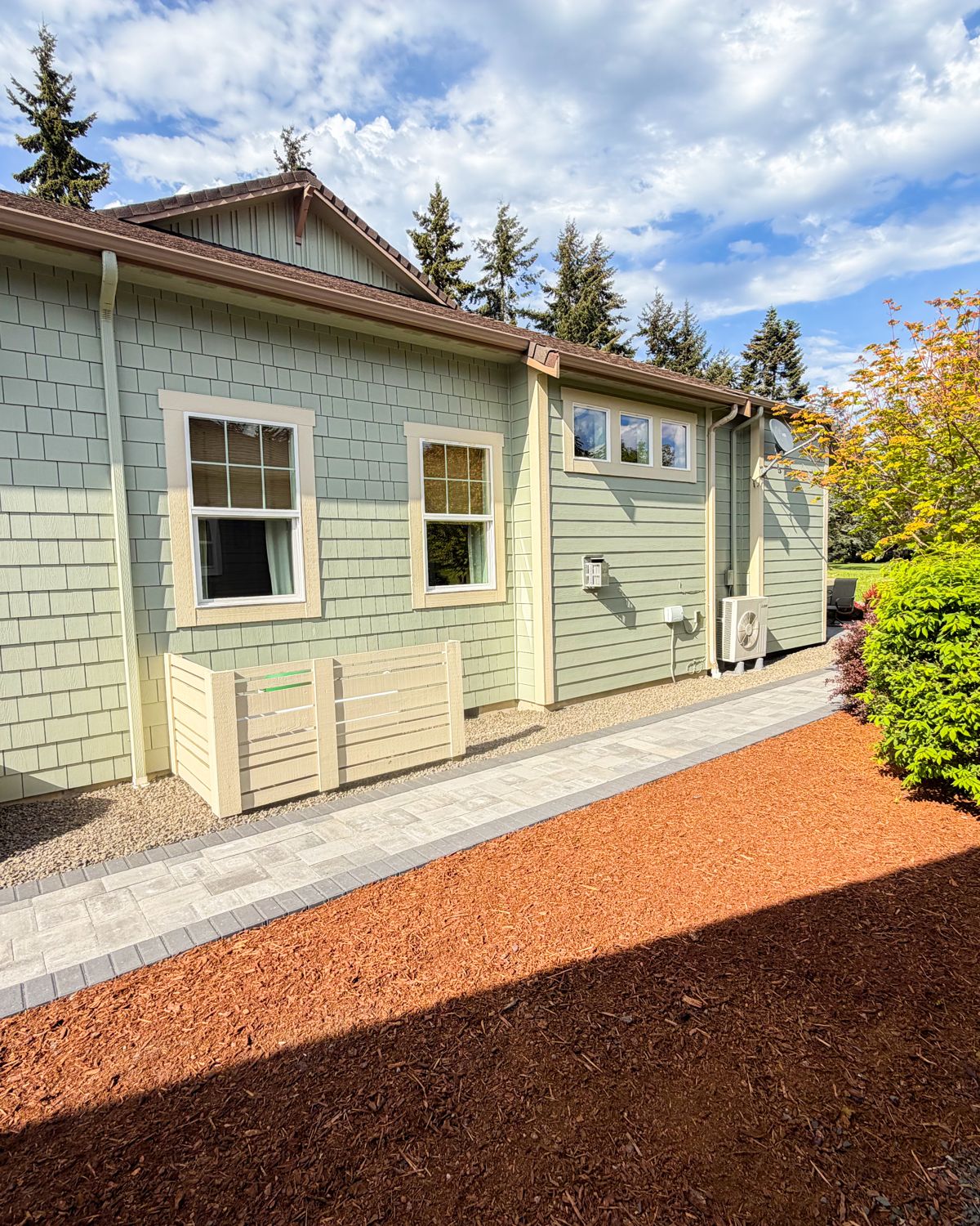 Paver walkway along the side of a sage-green house with fresh mulch beds