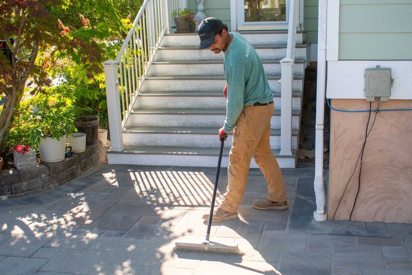 Crew member sweeping a finished paver patio at the base of entry stairs