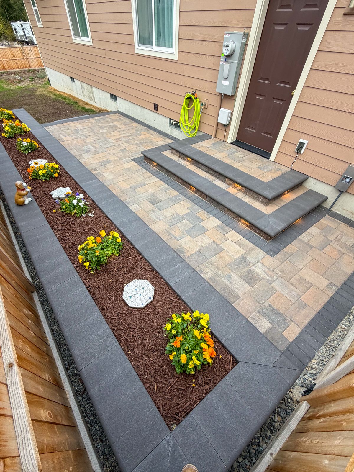 Paver patio with lit charcoal steps to a back door and a long bordered flower bed