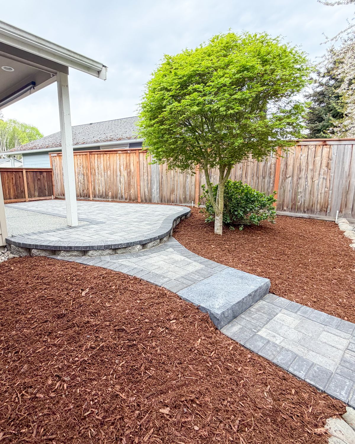 Curved gray paver patio off a covered porch with a walkway and stone step