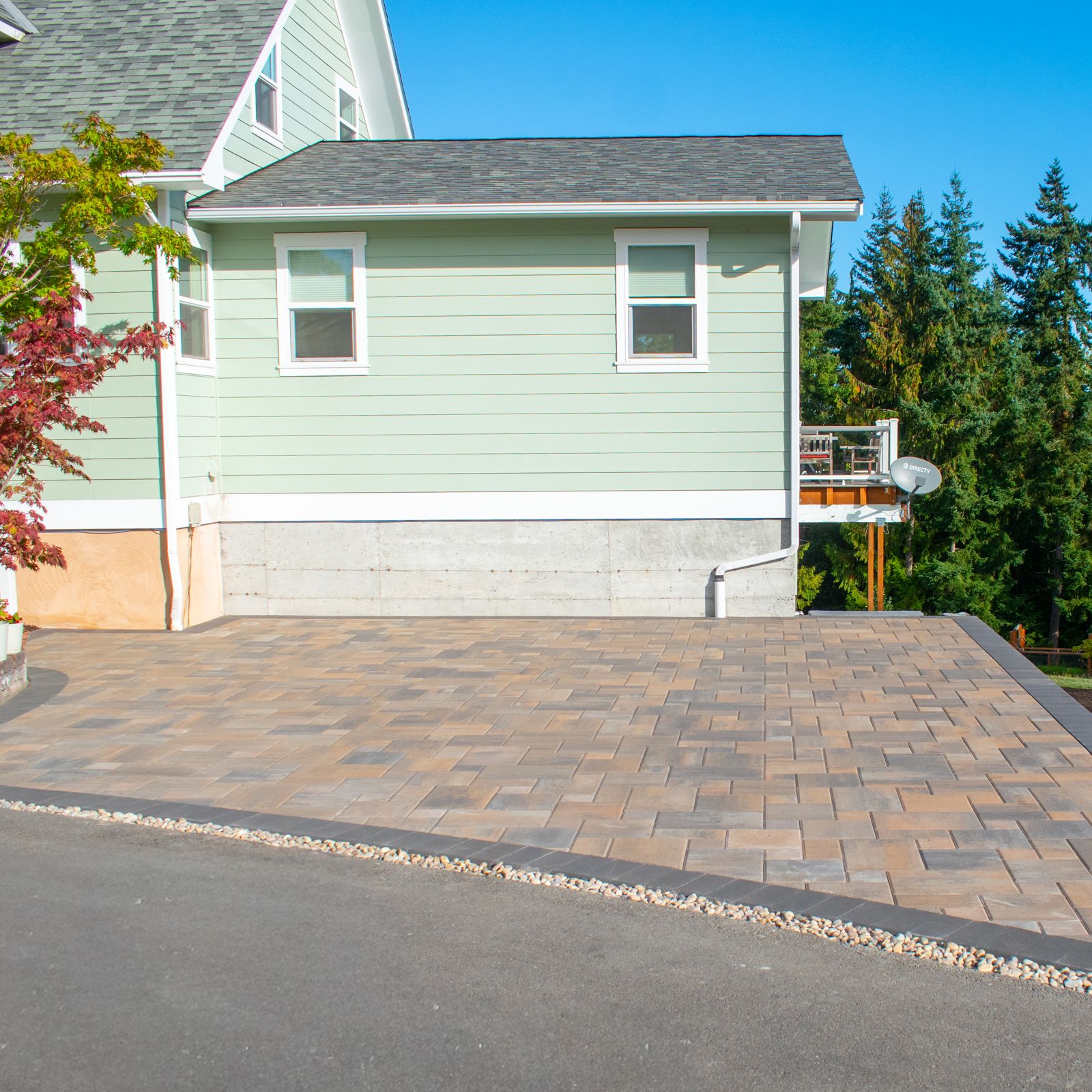 Large tan and gray paver patio with a charcoal border beside a sage-green house