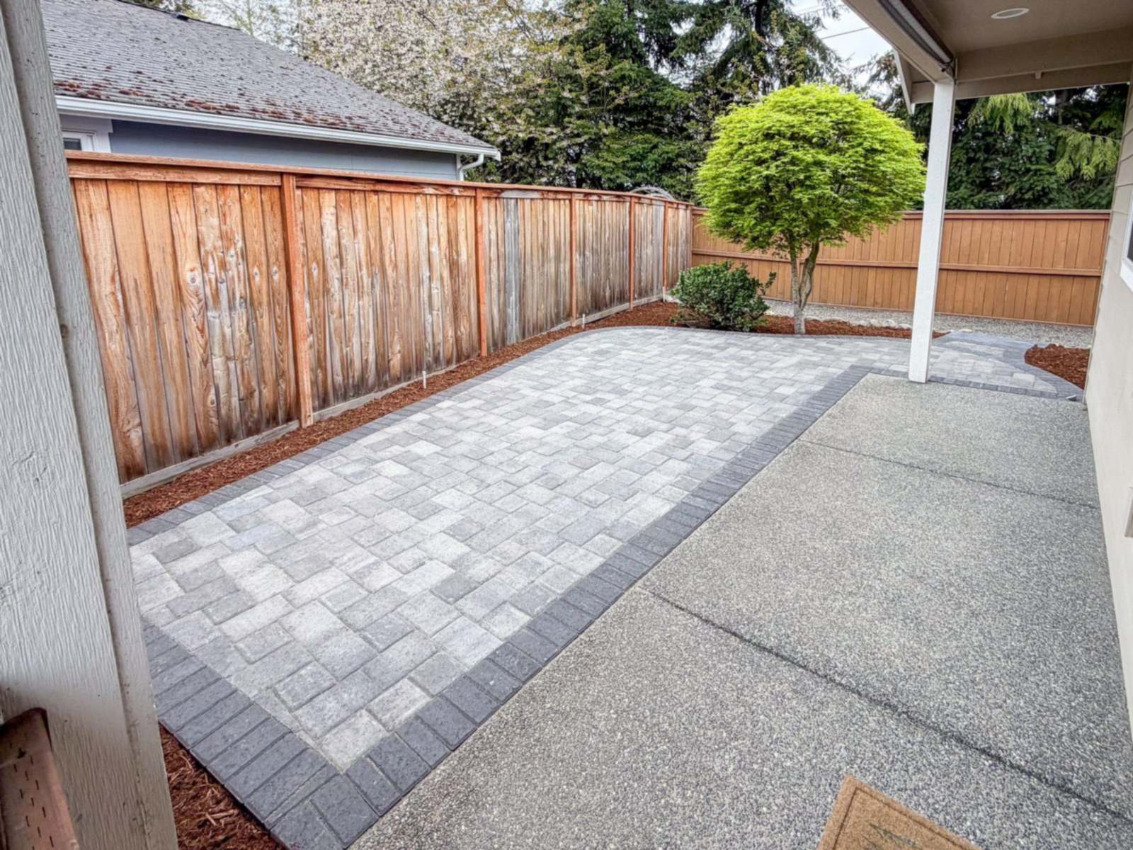 Gray paver patio with a charcoal soldier-course border along a cedar fence