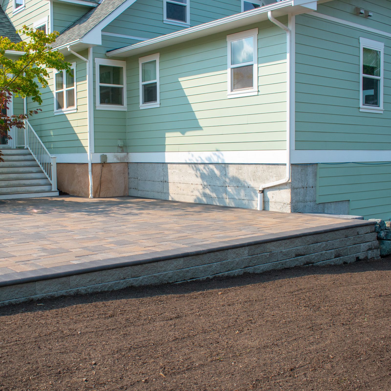 Raised paver patio held up by a block retaining wall next to the house