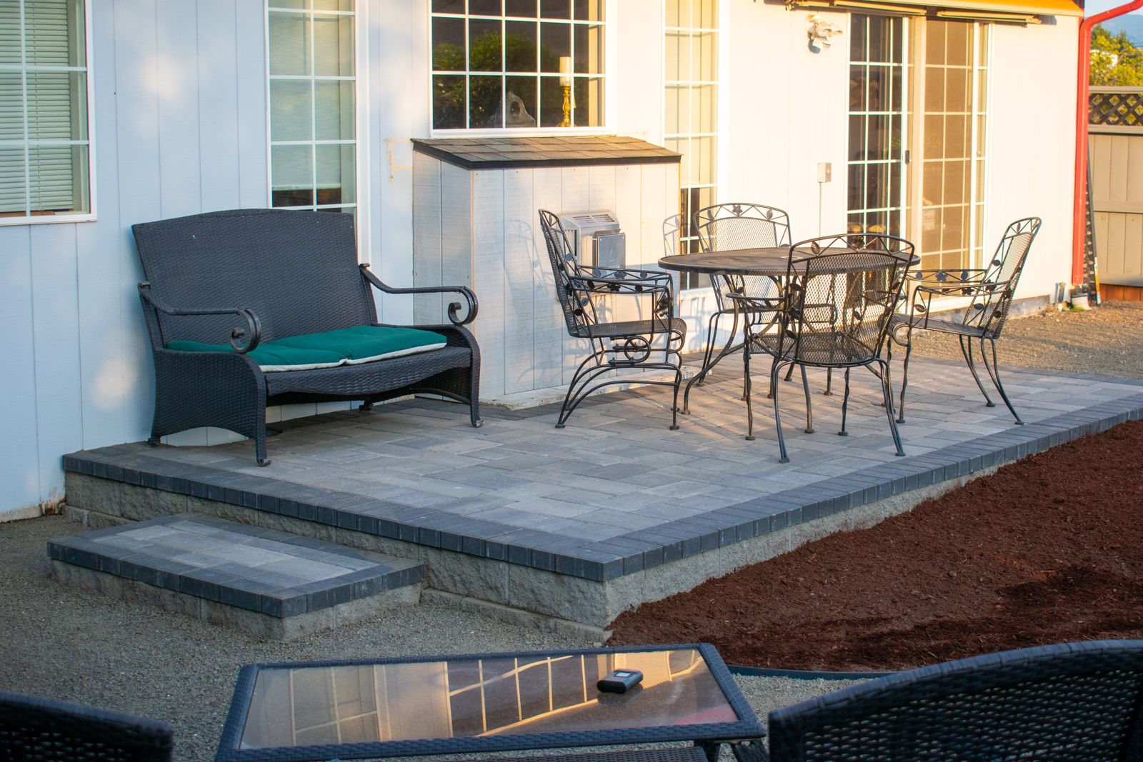 Raised gray paver patio with a charcoal border, a separate step and wrought-iron seating